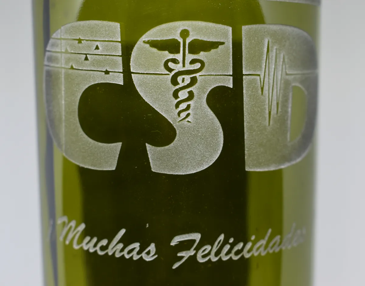 Botella de vidrio con el logo de CSD y la frase Muchas felicidades grabados con sand blast